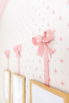 pink bows are hanging on the wall next to two framed pictures and a gold frame