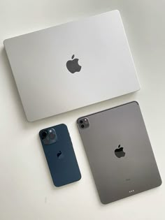 two apple laptops sitting next to each other on top of a white table in front of a computer