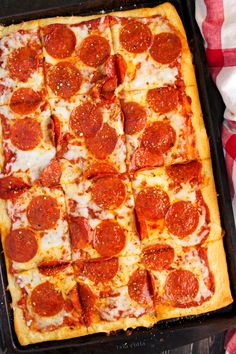 a square pepperoni pizza sitting on top of a black pan next to a red and white checkered table cloth