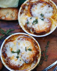 two small white bowls filled with cheese and sauce on top of a wooden table next to bread