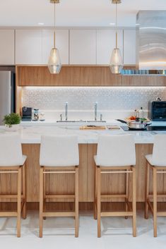 a kitchen with white counter tops and wooden stools next to an island in the middle