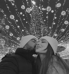 a man and woman kissing in front of a christmas tree with lights all around them