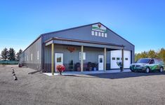 two cars are parked in front of a large metal building with multiple doors and windows