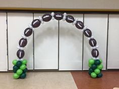 an arch made out of balloons with footballs and green balls on it in front of a wall