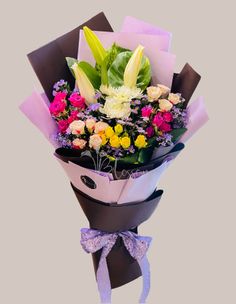 a bouquet of flowers is wrapped in brown paper and tied with a purple ribbon, on a gray background