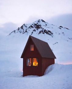 a small cabin in the middle of a snowy field with a mountain behind it at night