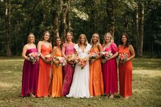 a group of women standing next to each other in front of trees holding bouquets