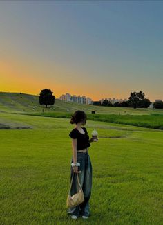 a woman standing on top of a lush green field holding a bag and a cell phone