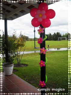 some pink and green balloons are hanging from a pole in the grass near a pond