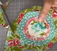 someone is cutting fabric with scissors on the floor next to a flowered place mat