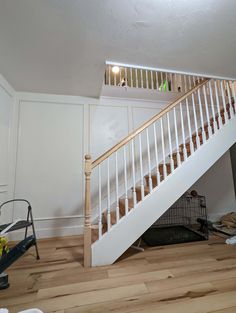 an empty room with white stairs and hard wood flooring