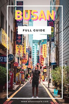 a man standing in the middle of an alley way with neon signs and buildings behind him