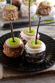 four desserts on a black plate with green apples in the middle and small sprouts sticking out of them