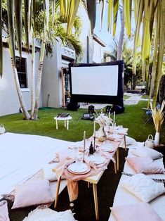 an outdoor movie is set up on the lawn with pink and white linens, while palm trees are in the background