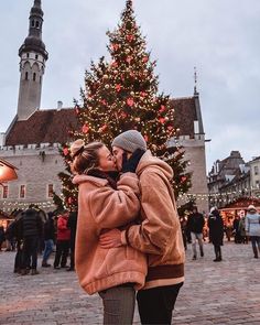 a man and woman kissing in front of a christmas tree with lights on the trees