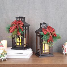 two christmas lanterns with pine cones and red plaid bows are sitting on a wooden table