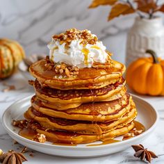 a stack of pancakes topped with whipped cream and pecans on a white plate next to pumpkins