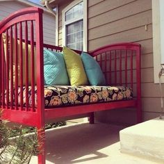 a red bench sitting on the side of a house next to a planter filled with flowers