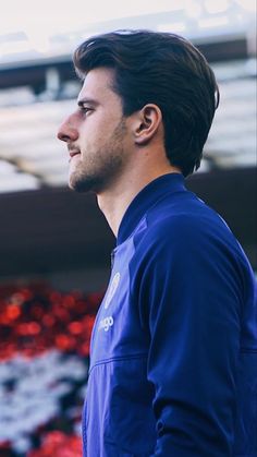 a man standing in front of a stadium full of red and white flowers with his head turned to the side