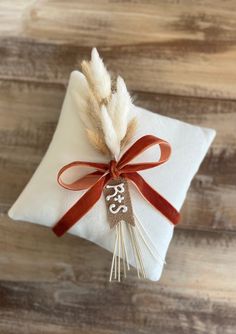 a white pillow with a red ribbon tied around it and a decorative feather on top