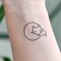 a small black and white fox tattoo on the left wrist, with a crescent moon behind it