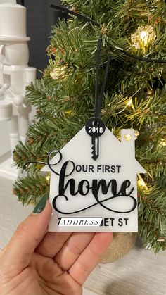 someone holding up a house ornament in front of a christmas tree that says our first home