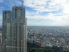 an aerial view of a city with skyscrapers and trees in the foreground, under a partly cloudy sky