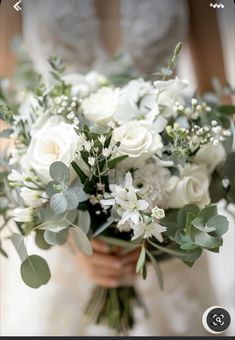 a bride holding a bouquet of white flowers and greenery