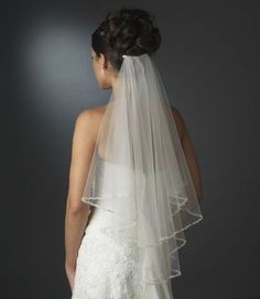 the back of a bride's wedding dress with a veil on her head and shoulder