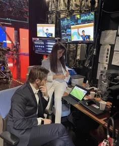 two people are sitting in front of televisions and talking on their cell phones while one person sits at a desk with a laptop