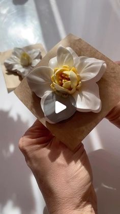 a person holding a piece of paper with a flower on it and another object in the background