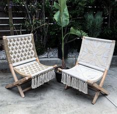 two lawn chairs sitting next to each other near a potted plant and some trees