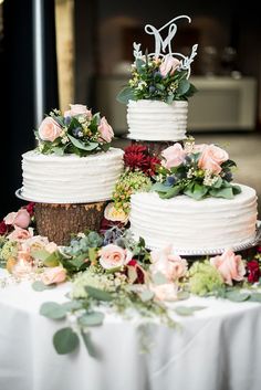 three tiered wedding cake sitting on top of a table with flowers and greenery