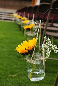 sunflowers and baby's breath in mason jars line the aisle of an outdoor ceremony