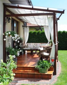 an outdoor patio with white curtains and flowers on the steps leading up to the deck