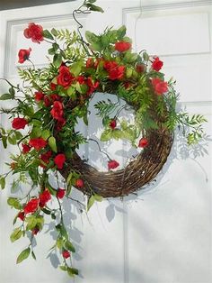 a wreath with red flowers and greenery hanging from the side of a white door