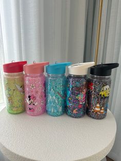 five different colored glass jars sitting on top of a white table next to a window