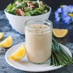 a bowl of salad next to a small glass jar filled with dressing on a plate