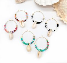 four pairs of hoop earrings with shells and beads on white surface next to seashell