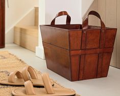 a pair of sandals sitting on the floor next to a brown bag and slippers