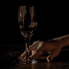 a hand reaching for a wine glass on a table in the dark with only one hand