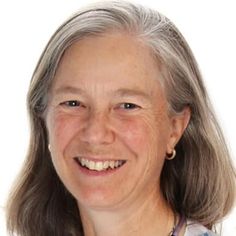 an older woman with grey hair smiling at the camera while wearing a blue and white checkered shirt