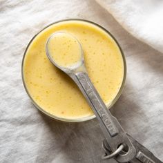 a spoon in a glass bowl filled with yellow liquid on top of a white cloth