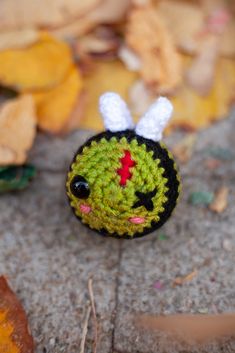 a small crocheted toy sitting on top of a cement ground next to leaves