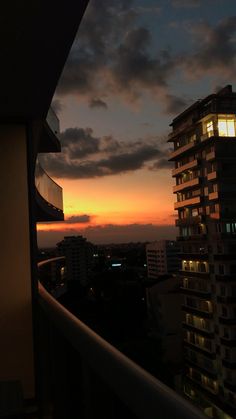 the sun is setting over some buildings in the cityscape as seen from an apartment balcony