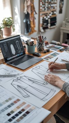 a person sitting at a desk with a laptop and drawing on paper next to it