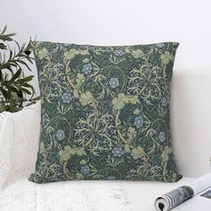 a green and blue pillow sitting on top of a white couch next to a plant