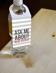 a bottle of water sitting on top of a wooden table next to a sign that says ask me about real estate