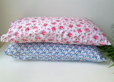 two pillows sitting next to each other on top of a white table near a potted plant