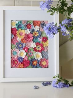 there is a white frame with crochet flowers in it and some blue flowers